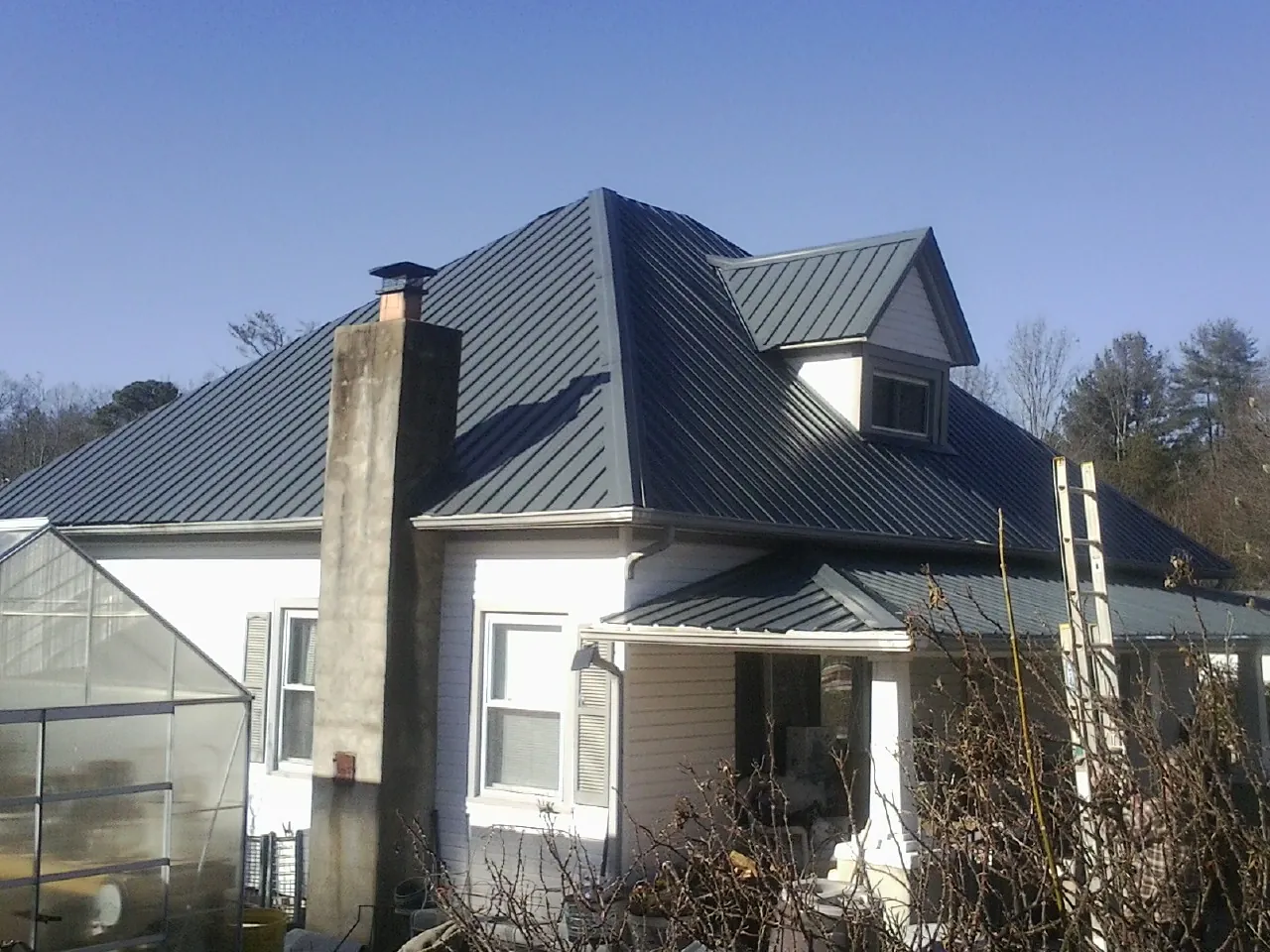 Dark blue standing seam metal roof on a white farmhouse with dormer — Slate & Tile Roof Repair by Roofing Brothers in Meadow