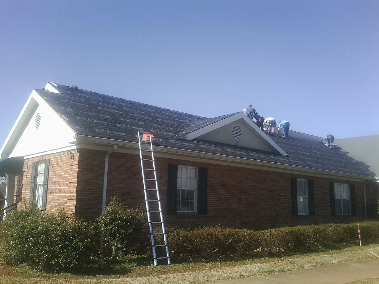 Crew tearing shingles off a brick ranch roof with a ladder set — Emergency Roof Repair work by our crew in Meadow