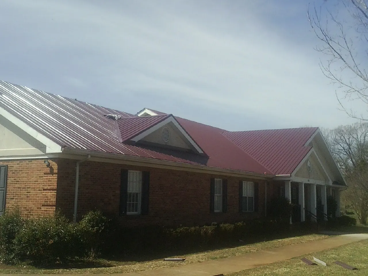 Red metal roof with gabled entries on a long brick building, from a Hail Damage Roof Repair job in Meadow