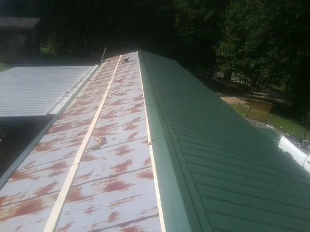 Old rusted panels beside newly installed green metal roofing — Wind Damage Roof Repair by Roofing Brothers in Meadow