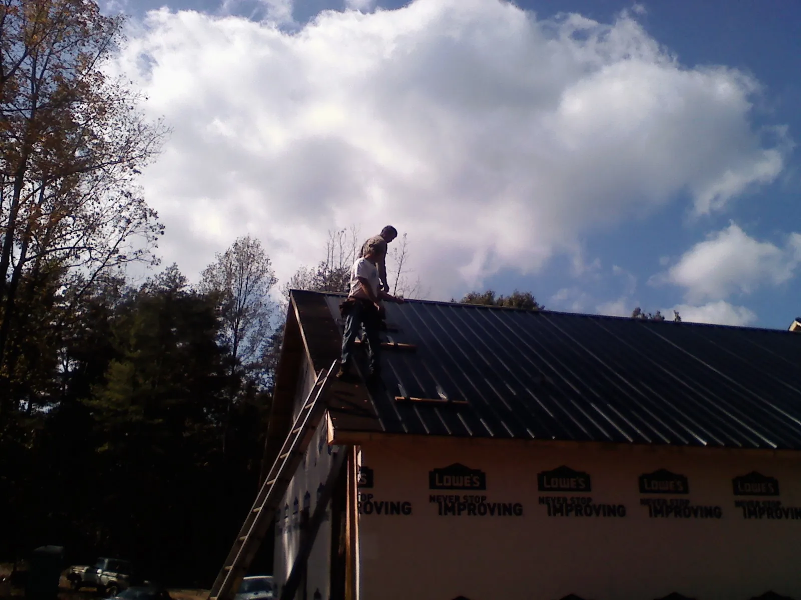 Roofer fastening dark metal panels high against a cloudy sky, from a Roof Inspection job in Meadow