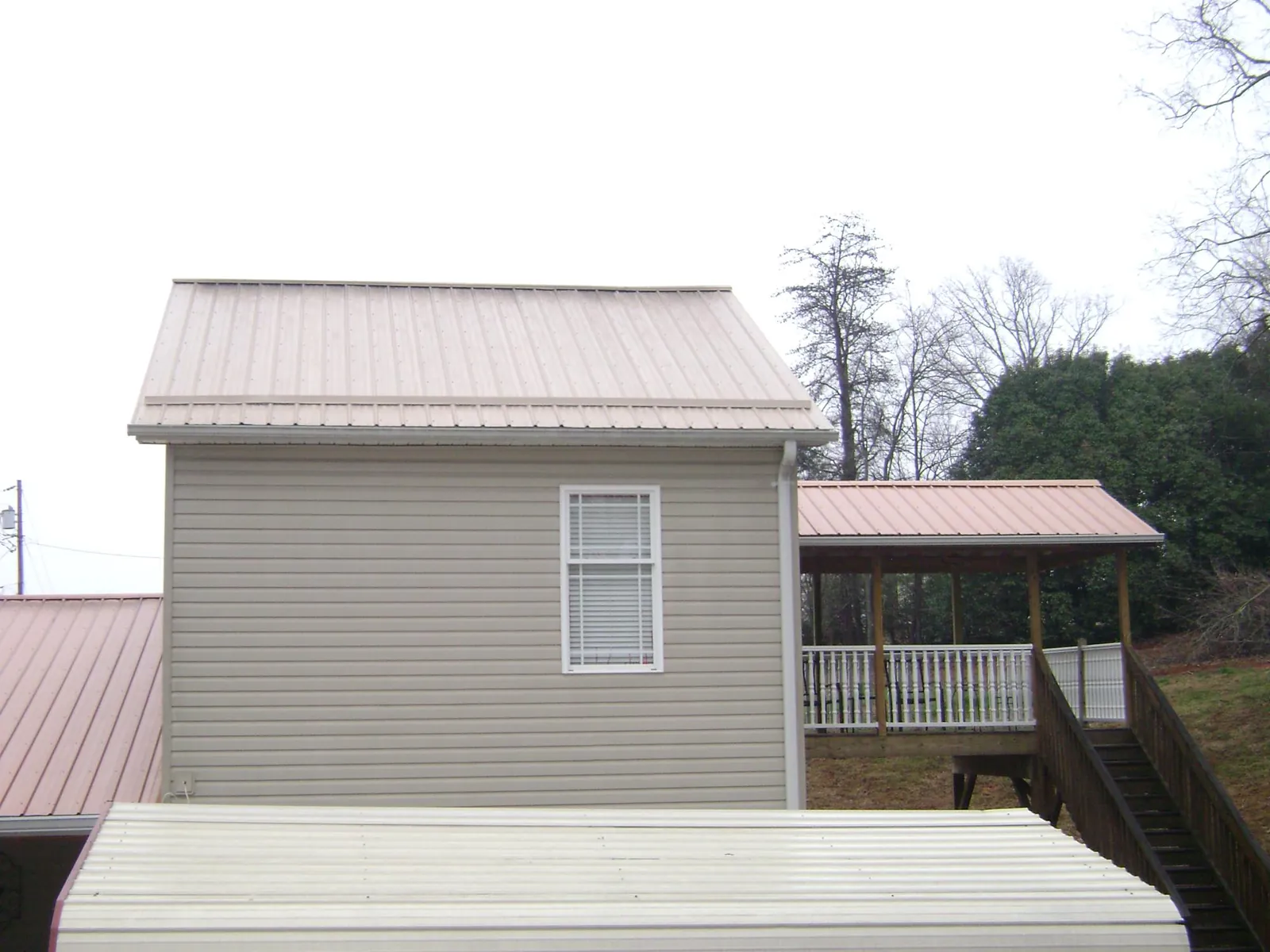 Tan metal roofs on a two story addition and attached porch, from a Roof Replacement job in Meadow